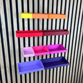 Organizer Boxen für Akustikpaneele in Gelb, Orange, Rot, Pink und Lila an einer Holz-Lamellenwand