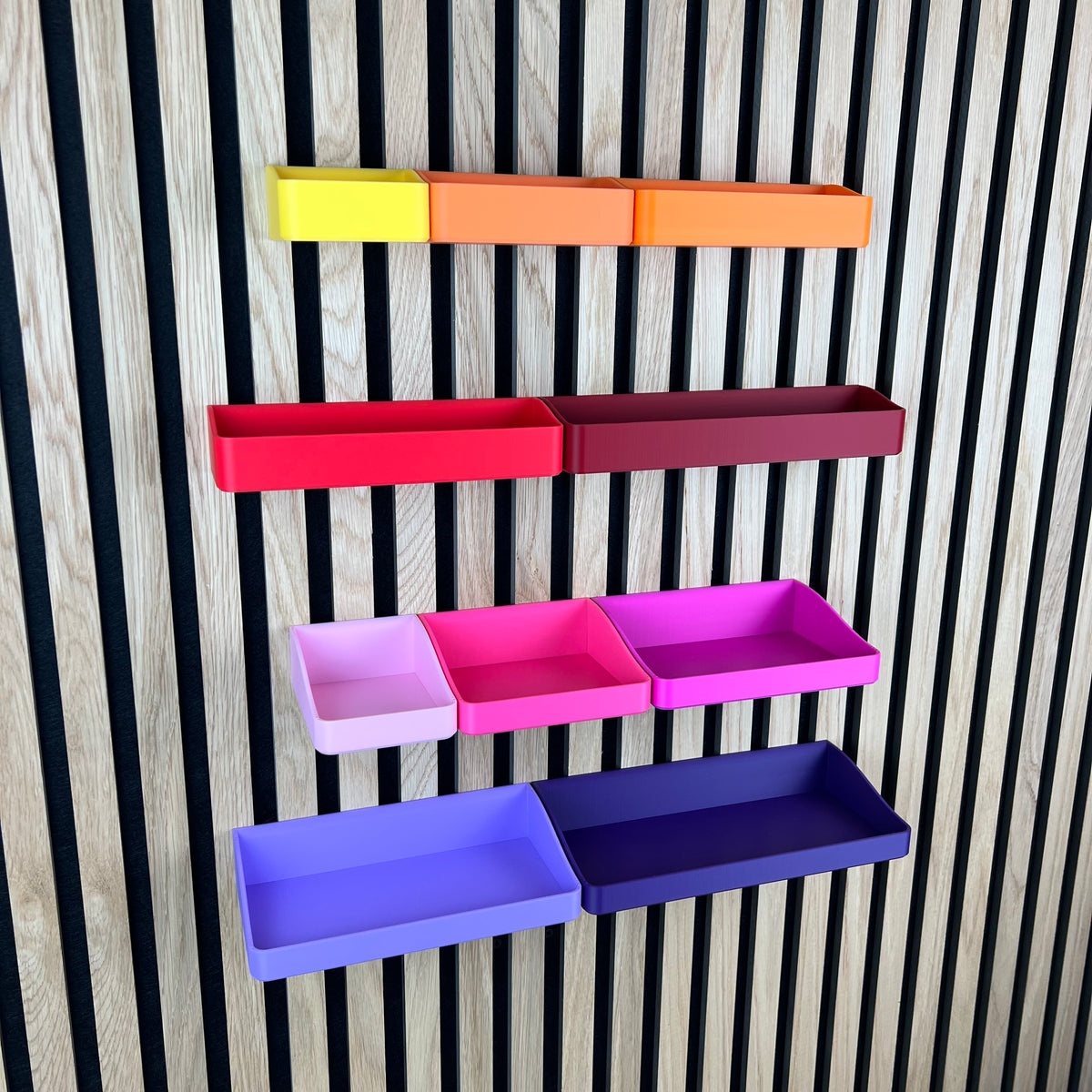 Organizer Boxen für Akustikpaneele in Gelb, Orange, Rot, Pink und Lila an einer Holz-Lamellenwand