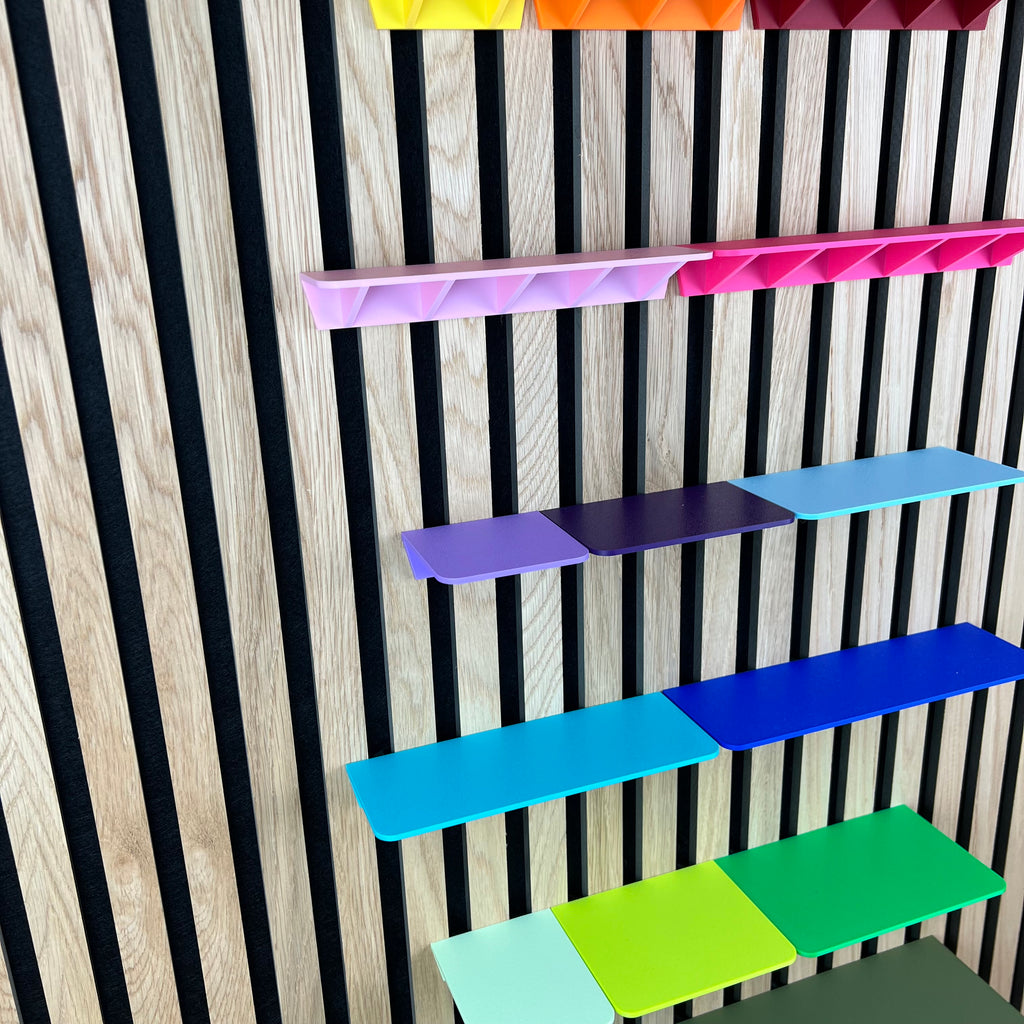 Ablagen in Rosa, Blau und Grün seitlich an einem Holz-Akustikpaneel