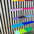 Ablagen in Rosa, Blau und Grün seitlich an einem Holz-Akustikpaneel