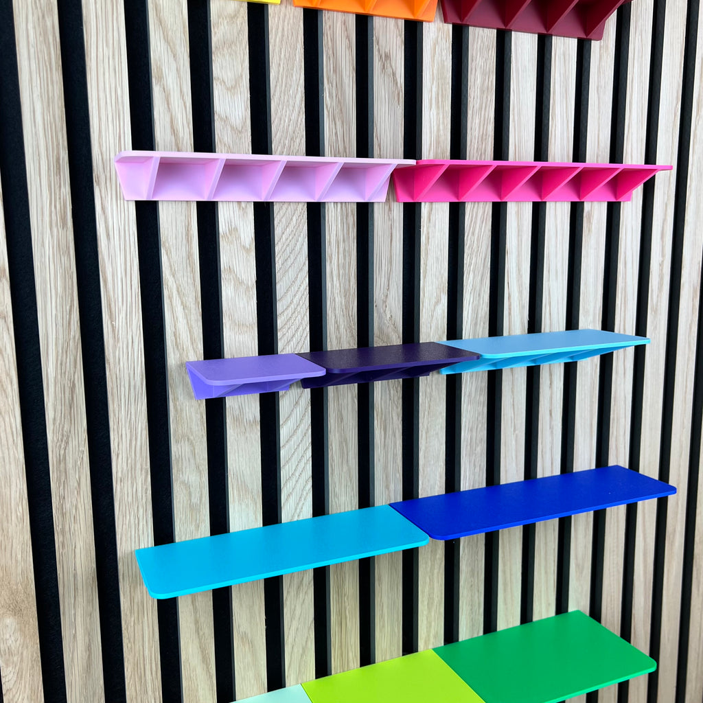 Ablagen in Pink, Lila und Blau an der Akustik-Lamellenwand von unten betrachtet