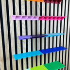 Ablagen in Pink, Lila und Blau an der Akustik-Lamellenwand von unten betrachtet