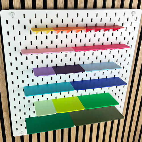 Weiße IKEA SKÅDIS Lochwand mit sechs farbigen 3D-gedruckten Ablagen in verschiedenen Breiten