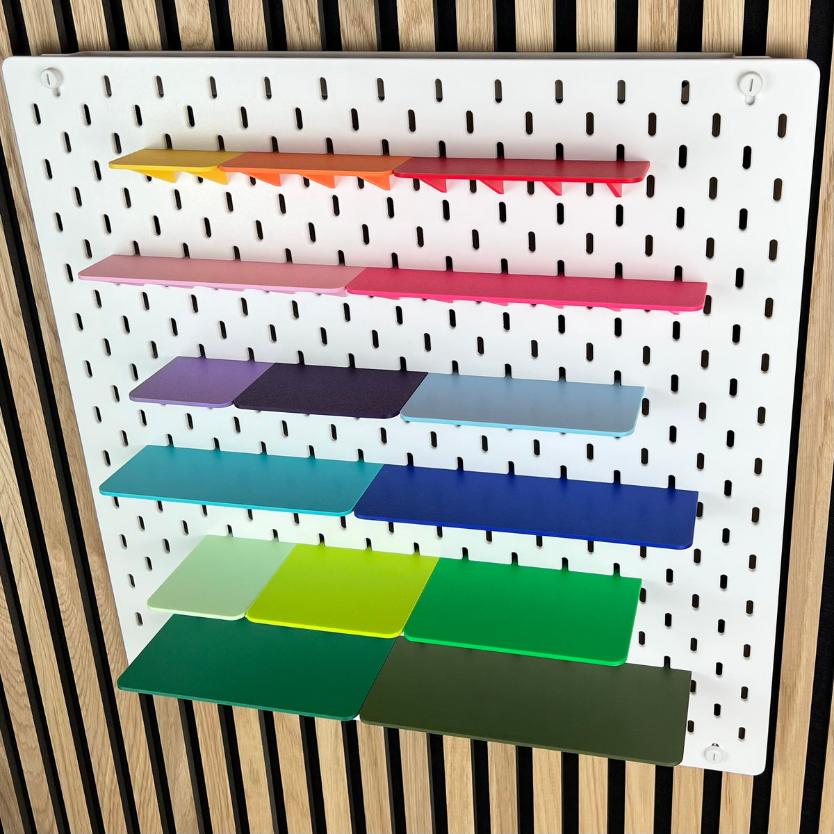 Farbige Ablagen für die IKEA SKÅDIS Lochwand, leicht seitliche Ansicht der sechs Regalreihen