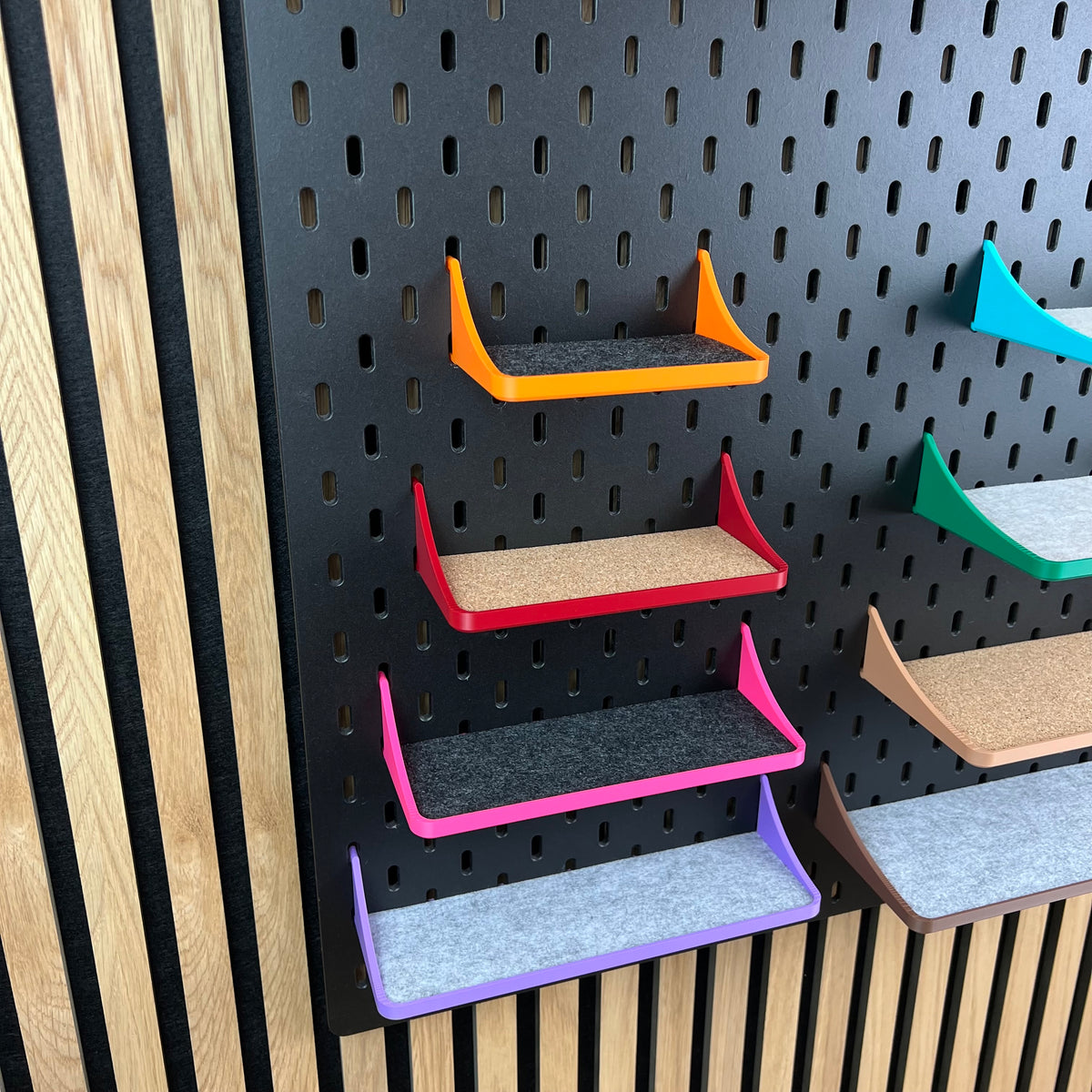 Vier Ablagen mit Rand in Orange, Rot, Pink und Lila untereinander an schwarzer Lochwand