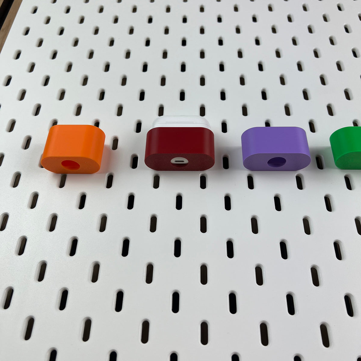 AirPods-Halterungen von oben an weißer Lochwand, Ladeöffnung im Boden erkennbar
