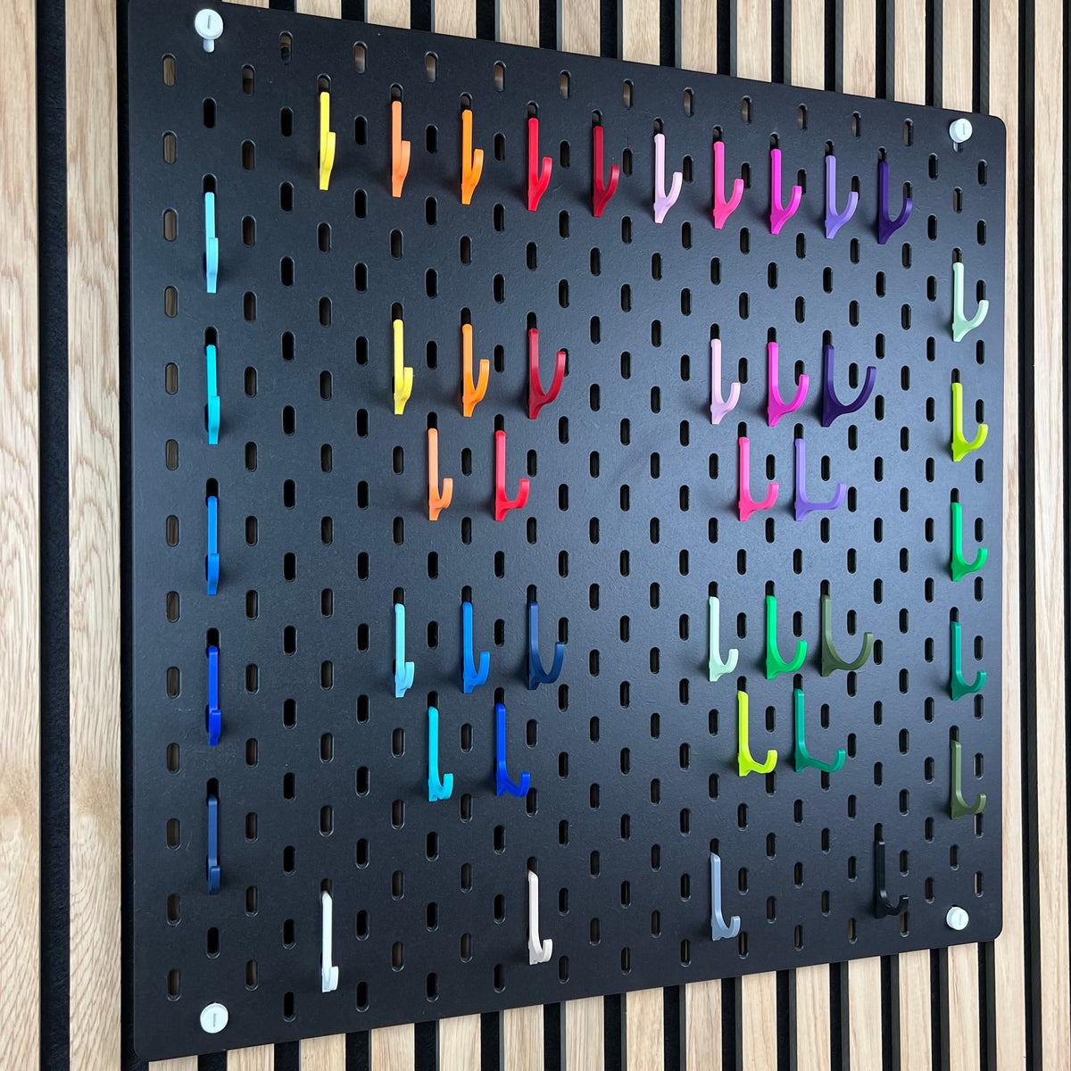 Schwarze IKEA SKÅDIS Lochwand mit farbigem Haken-Sortiment im Raster, Gesamtansicht vor Akustik-Holzwand