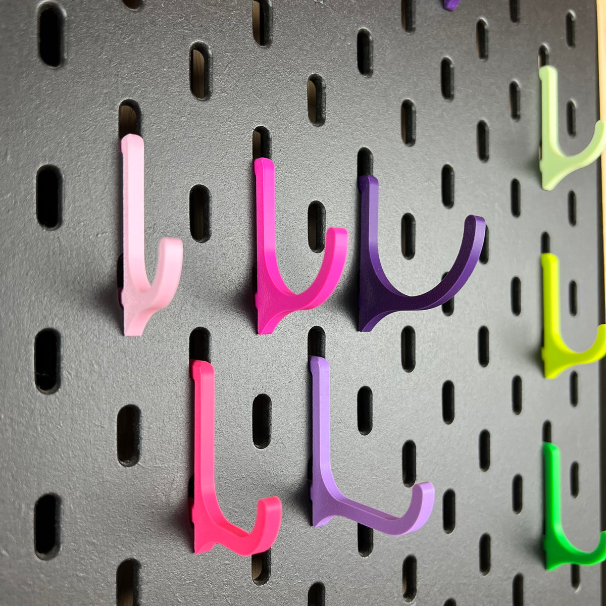 SKÅDIS Haken in Rosa, Magenta und Violett als Detailaufnahme an der schwarzen Lochwand