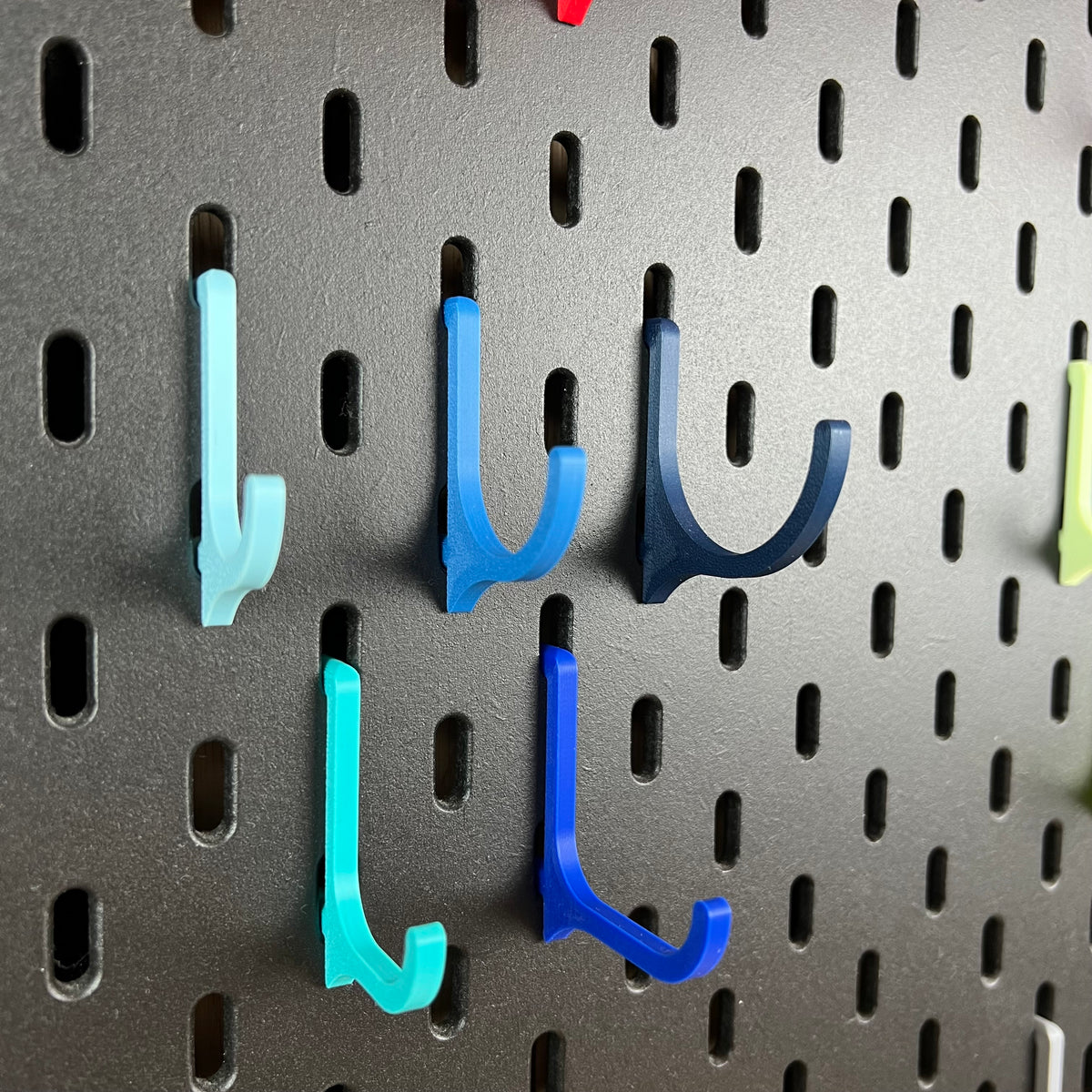 Blaue und türkise 3D-gedruckte Haken für die IKEA SKÅDIS Lochwand in zwei Längen