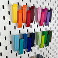 Bunte 3D-gedruckte Klipps an einer weißen IKEA SKÅDIS Lochwand, Nahaufnahme in Gelb, Orange, Rot und Violett