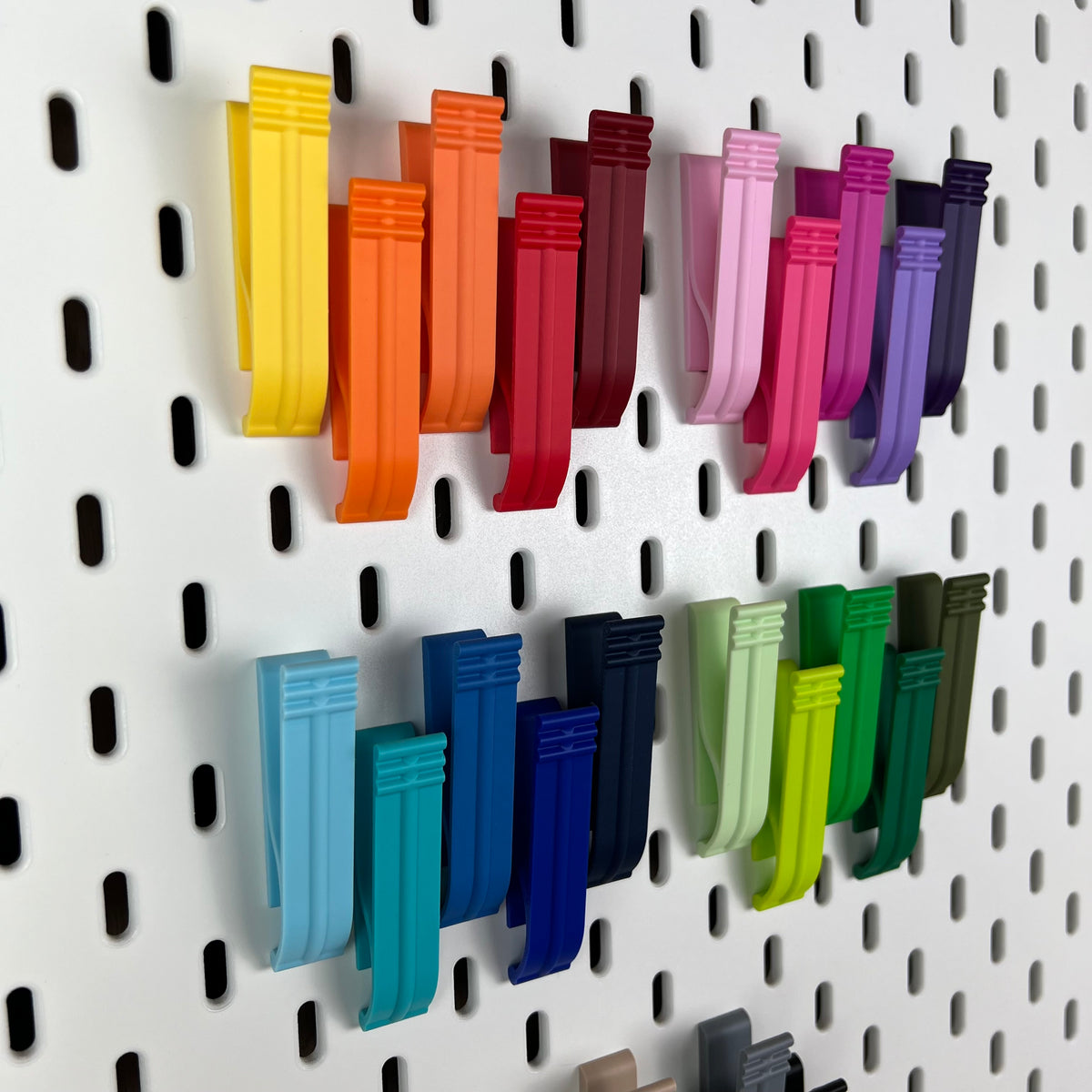 Bunte 3D-gedruckte Klipps an einer weißen IKEA SKÅDIS Lochwand, Nahaufnahme in Gelb, Orange, Rot und Violett