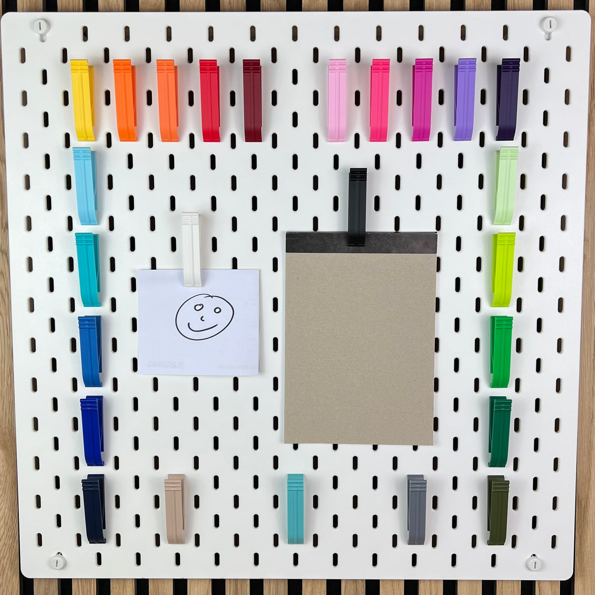 IKEA SKÅDIS Lochwand mit farbigen Klipps als Rahmen, Notizzettel und Brett daran befestigt