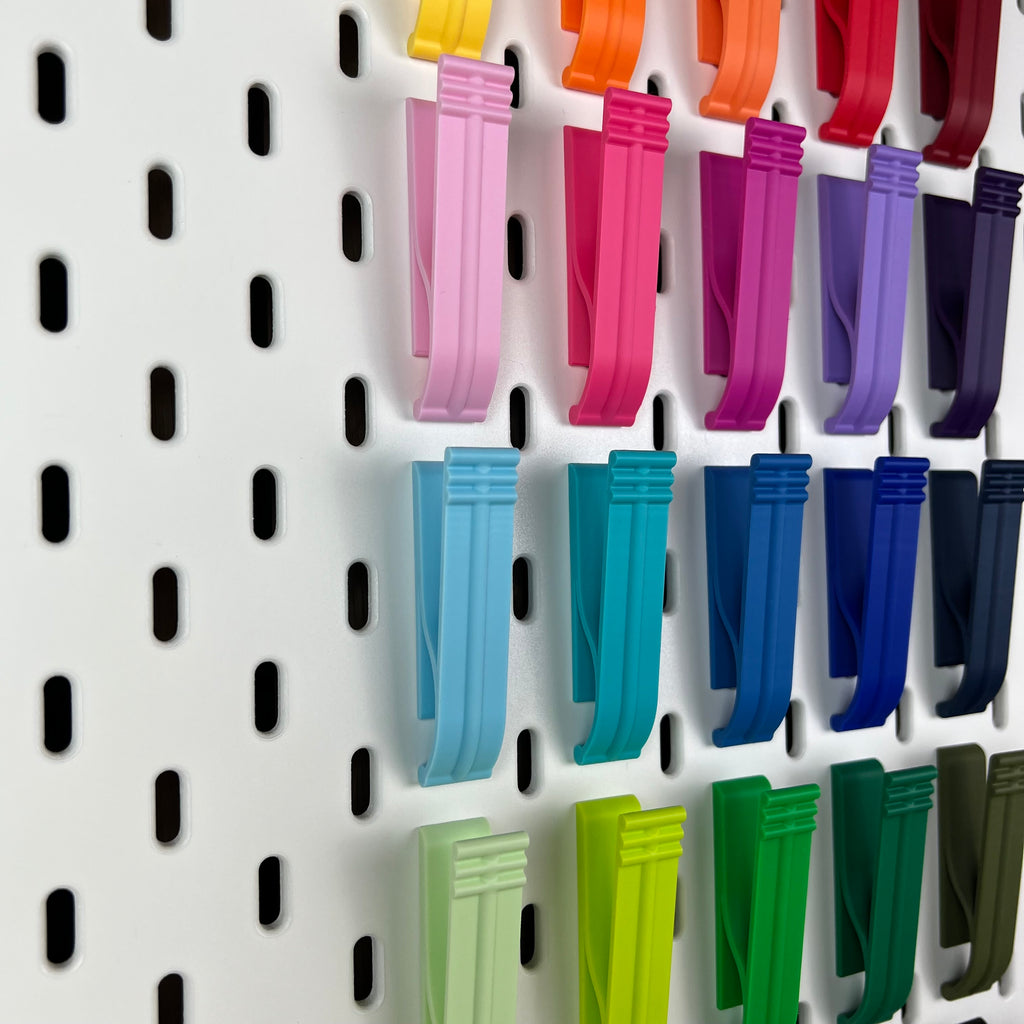 Detailaufnahme der Klipp-Halterungen in Rosa, Magenta, Türkis und Grün an der SKÅDIS Lochwand