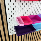 Pinke, magenta und violette SKÅDIS Boxen an der Lochwand, Blick von schräg unten in die Boxen