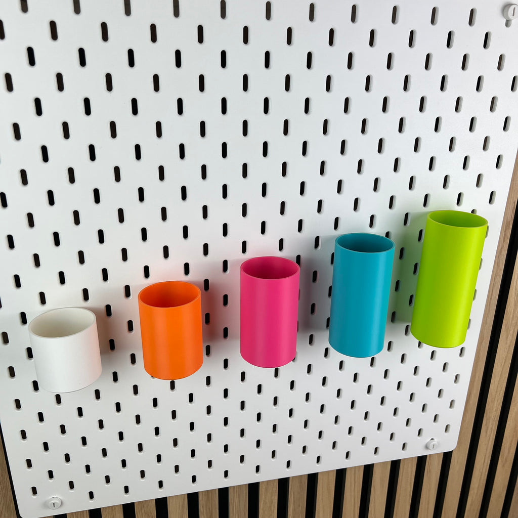 Nahaufnahme runder SKÅDIS Boxen in Weiß, Orange, Pink, Blau und Grün an weißer Lochwand