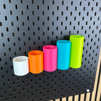 Runde Boxen in Weiß, Orange, Pink, Blau und Grün als Nahaufnahme an schwarzer Lochwand