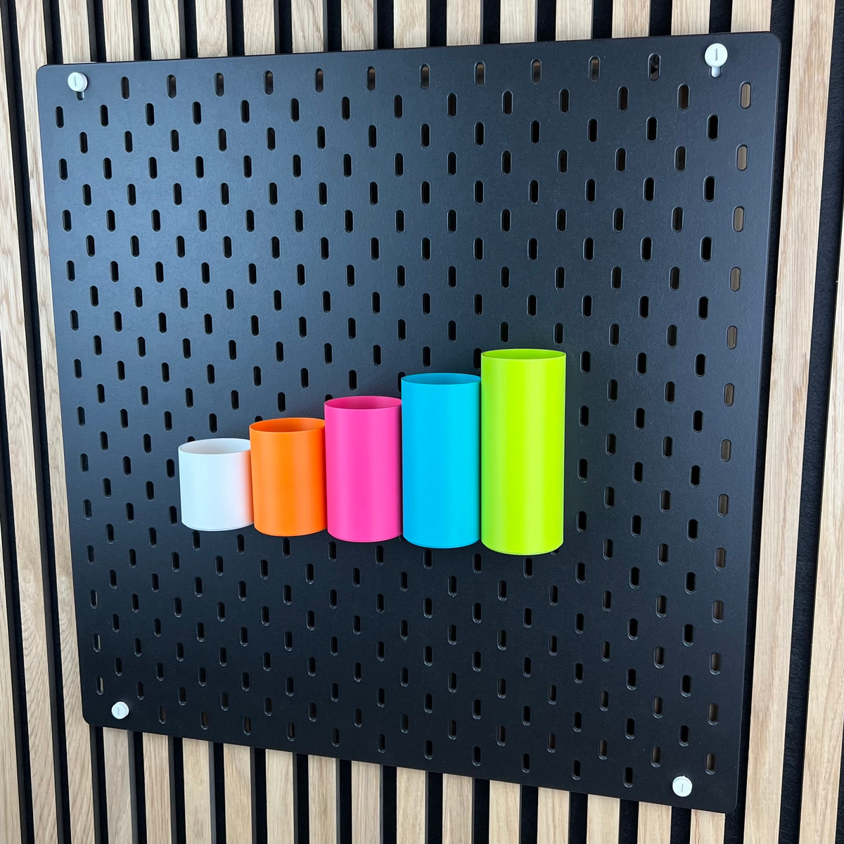 Schwarze IKEA SKÅDIS Lochwand mit fünf runden Boxen, perspektivische Ansicht vor Holzwand
