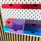 Geöffnete violette SKÅDIS Schublade zeigt den Innenraum, umgeben von Schubladen in Pink und Blau