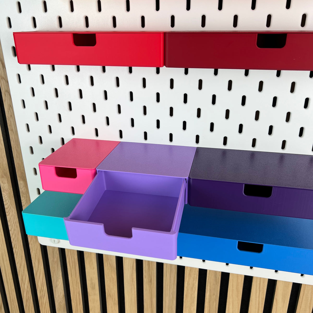 Geöffnete violette SKÅDIS Schublade zeigt den Innenraum, umgeben von Schubladen in Pink und Blau