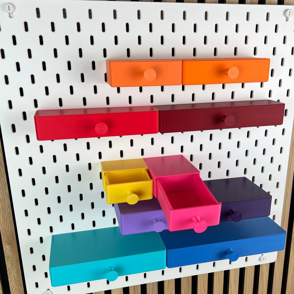 Zwei geöffnete SKÅDIS Schubladen in Gelb und Pink zeigen die nutzbare Innenhöhe