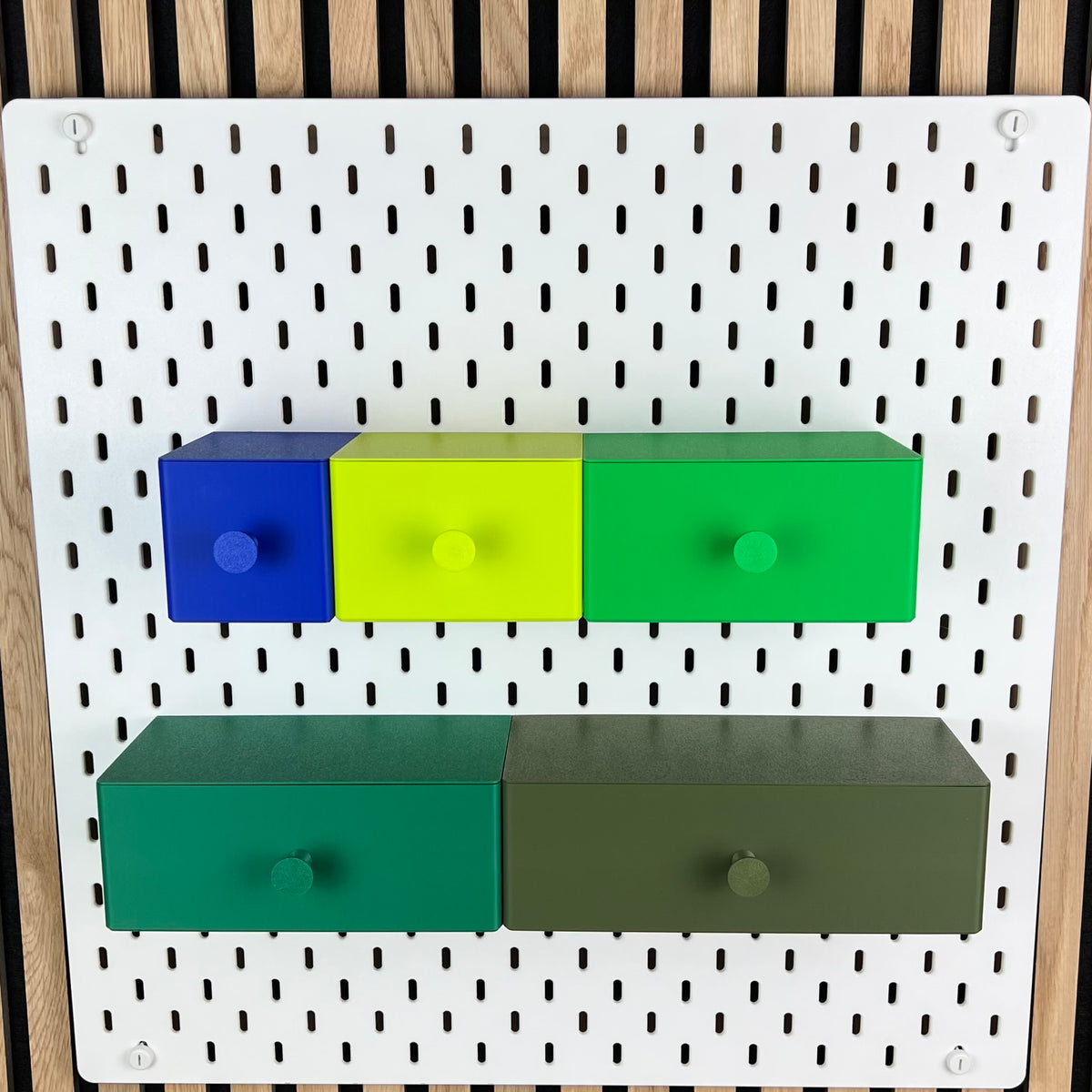 Fünf SKÅDIS Schubladen in Blau, Leuchtendes Grün und weiteren Grüntönen an der weißen Lochwand