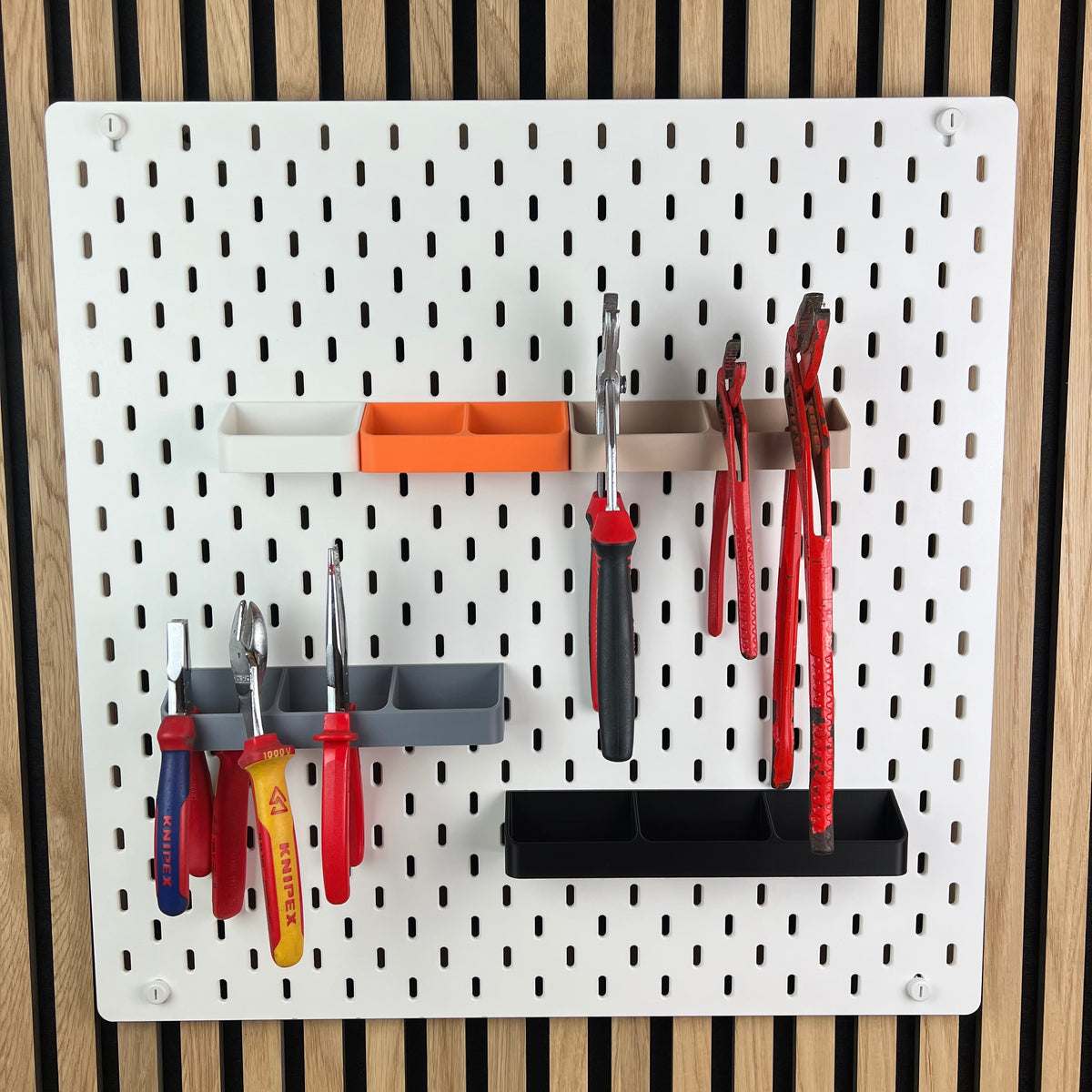 Weiße SKÅDIS Lochwand mit Zangenhalterungen und Werkzeug vor Akustikpaneel aus Holz
