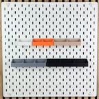 Fünf Zangenhalterungen in Weiß, Orange, Beige, Grau und Schwarz an weißer SKÅDIS Lochwand