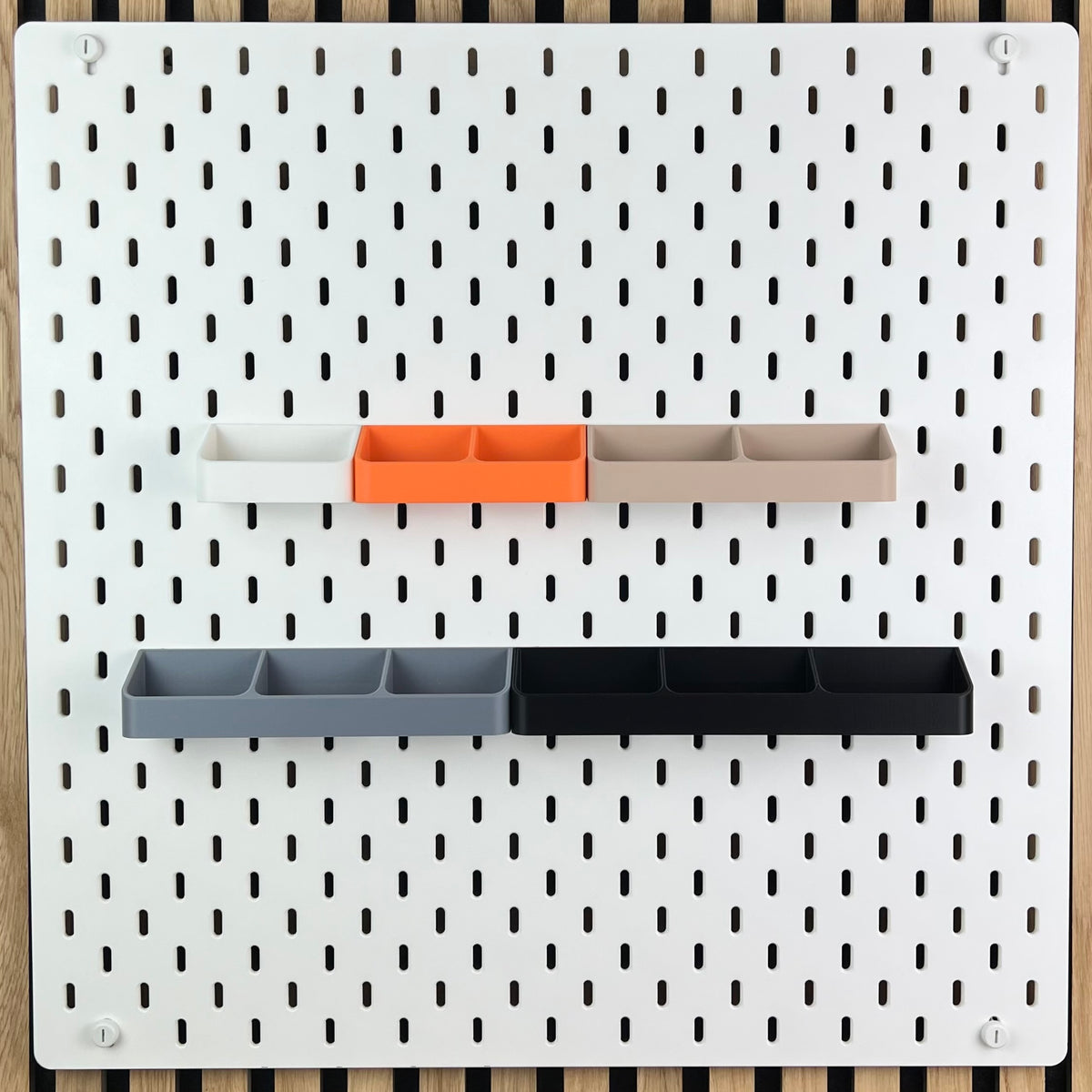Fünf Zangenhalterungen in Weiß, Orange, Beige, Grau und Schwarz an weißer SKÅDIS Lochwand
