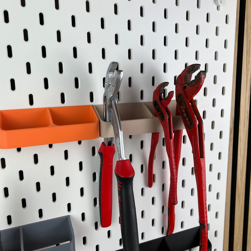 Detailaufnahme einer beigen Zangenhalterung mit drei roten Zangen an weißer SKÅDIS Lochwand